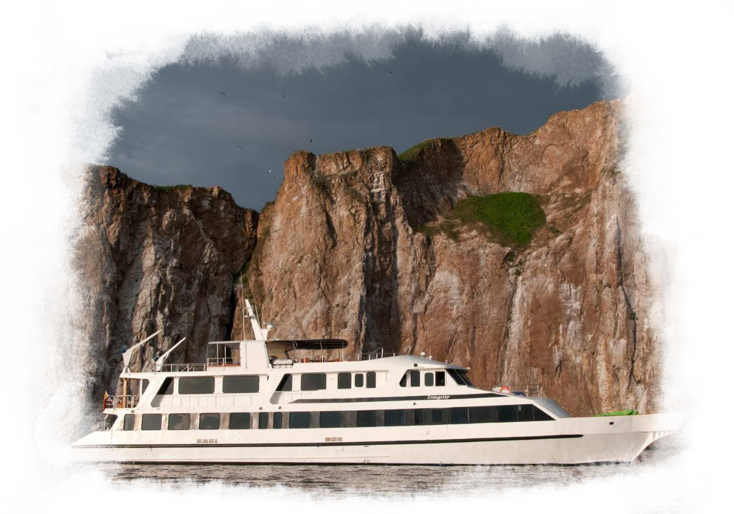 An outside view of the integrity ship sailing past a large escarpment.